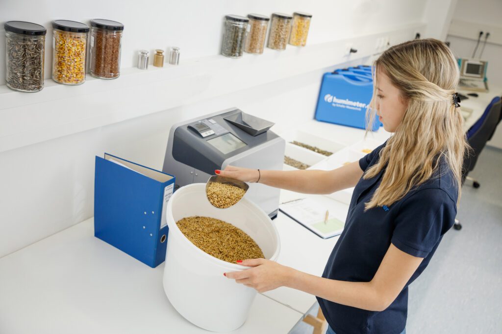 The employee takes a shovel full of grain from the plastic bucket.